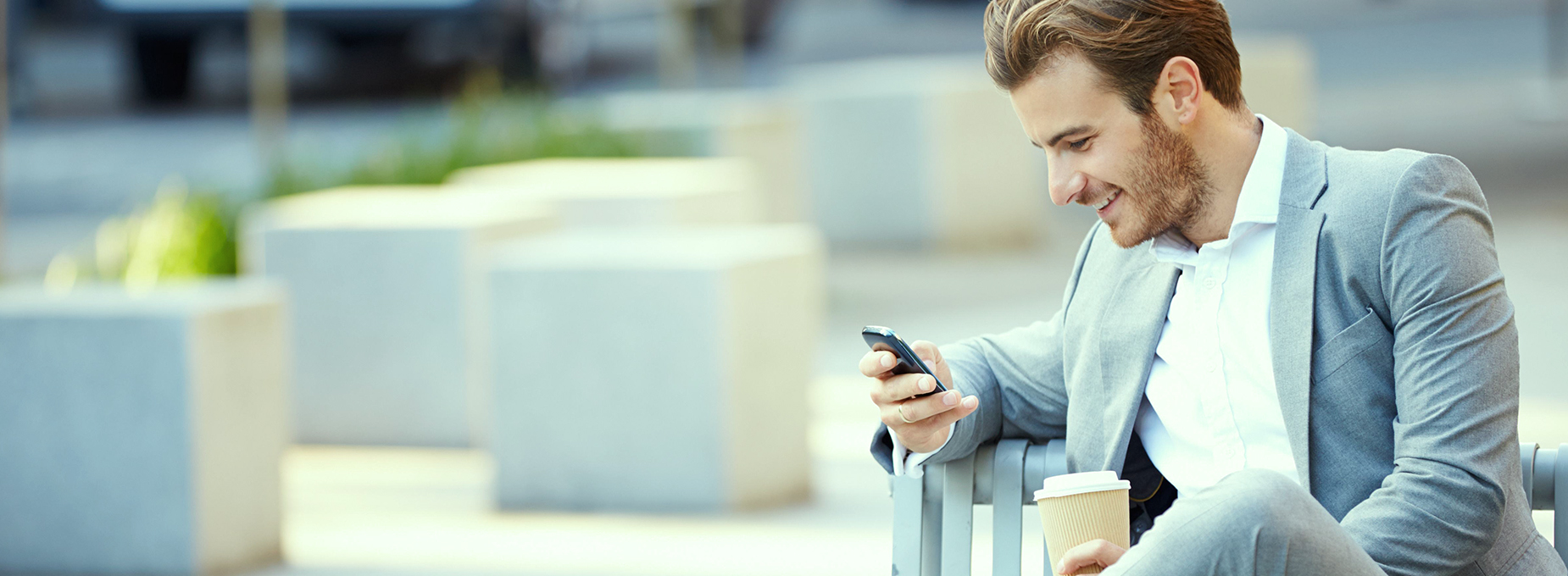 Businessman On Park Bench With Coffee Using Mobile Phone